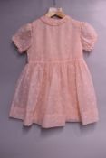 A 1950s early-years childrens dress in baby pink Bri-Nylon, comprising of two dresses to be worn