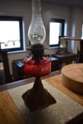 A Victorian cast-metal and cranberry glass oil lamp, the cranberry glass reservoir raised on a