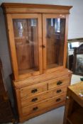 An Edwardian glazed pine bookcase over chest of drawers, having a moulded cornice and plain freize