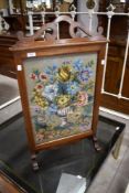 An early 20th century needlework firescreen, having a scrolled pierced surmount over the floral