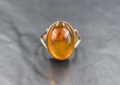 A Baltic amber cabochon ring in a collared mount to split shoulders on a yellow metal loop, no marks