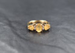 A 9ct gold citrine trilogy ring having two pairs of interspersing diamond chips, all in a raise claw