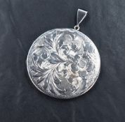 A large silver locket of slim circular form having engraved floral scroll decoration to front,
