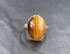 A Tigers eye cabochon ring, the oval stone in a collared mount on a yellow metal loop stamped 9ct,