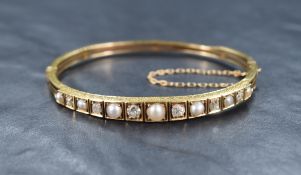 A hinged gold bangle having diamond and split pearl decoration to front panel, no marks but presumed