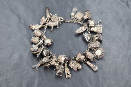 An early 20th century white metal charm bracelet, having thirty-five charms including a