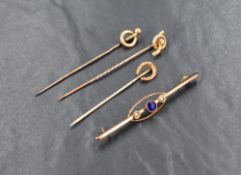 Three yellow metal stick pins, comprising a diamond set knot motif marked 15ct, another of a knot