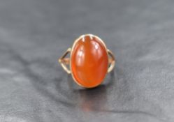 A carnelian cabochon ring, the oval stone in a collared mount to split shoulders on a yellow metal
