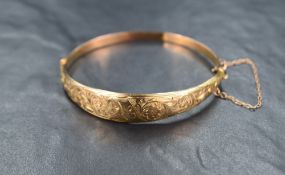 A 9ct gold hinged bangle, the tapered design having engraved floral and scroll decoration with a