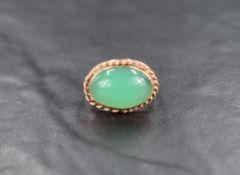 An oval jade style cabochon ring having a collared mount with twist wire decoration on a yellow