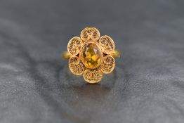 An oval citrine ring having an oval stone in a collared set filligree petal mount on a yellow