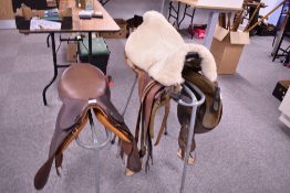Two leather saddles on two three legged saddle stands