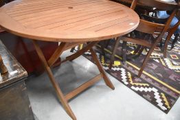 A modern stained teak circular garden table, with folding legs and central circular umbrella