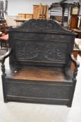 A Victorian oak box settle, with arched and scroll carved crest rail over a conforming panelled back