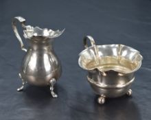 An Edwardian silver cream jug, having a Chippendale style rim with a broad spout opposed by a scroll