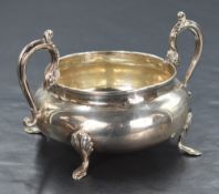 A George V silver sugar bowl, of bulbous form having decorative scroll handles, raised on four shell