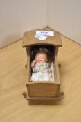 A small ceramic baby inside wooden cot, measures 8cm x 12cm.