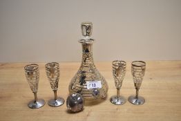A glass liqueur decanter having white metal overlay depicting flowers, with four glasses having
