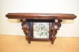 A solid mahogany bracket in the Aesthetic style, the centre tile decorated with foliage on a cream