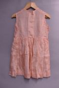 A 1950s early-years childrens dress in baby pink Bri-Nylon, comprising two dresses to be worn