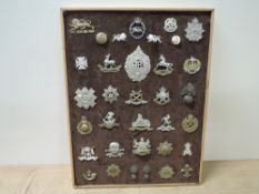 A framed board of 34 Military Helmet Plate, Cap Badges, Shoulder Badges etc including Argyll and