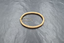 A high carat gold hinged bangle, of twisted design with safety chain, approx 8.9g
