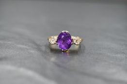 A yellow metal amethyst and diamond trilogy ring, the central oval cut amethyst measuring