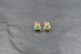 A pair of 9ct gold emerald stud earrings, the round cut emeralds within floral motif settings, 0.