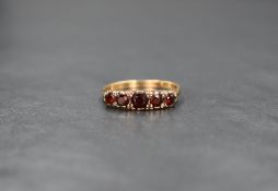 A yellow metal five stone garnet ring, having graduated stones in a gallery mount, marks worn,