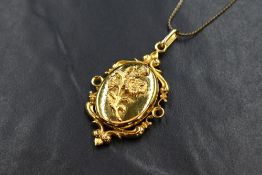 A yellow metal ornate locket, having a decorative pierced scroll setting with embossed flowers to