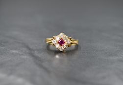 A yellow metal (presumed to be gold) ruby and diamond cluster ring, the central princess cut ruby