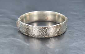 A 1960's silver hinged bangle, having decorative scroll engraving to one side and an extending