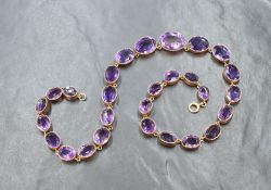 A yellow metal and amethyst rivière necklace, the graduated oval cut amethysts in a bezel