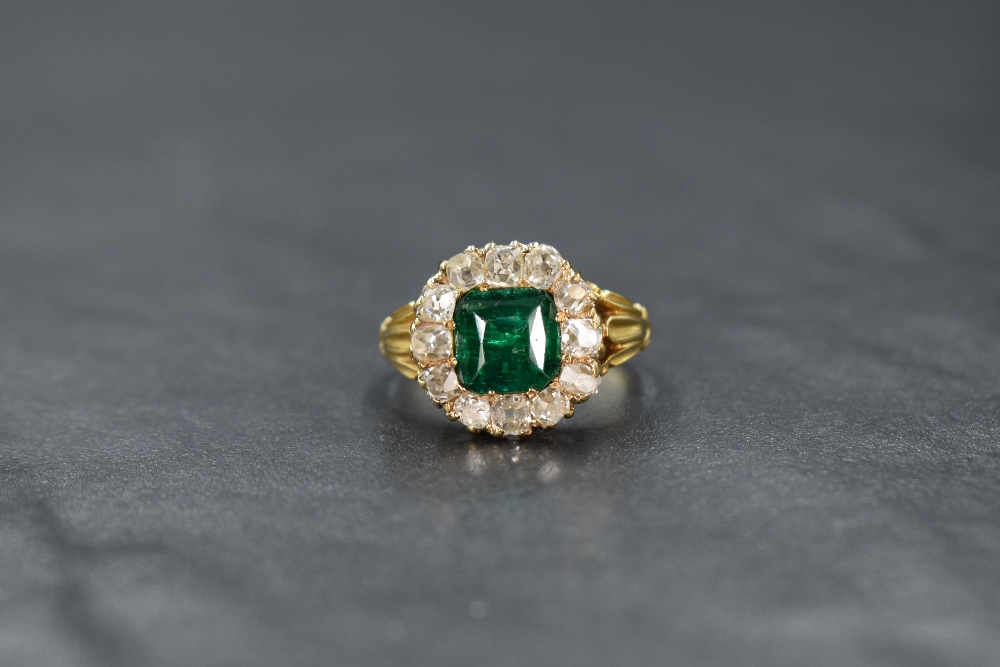 A yellow metal presumed gold emerald and diamond cluster ring, the central mixed cut emerald