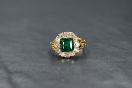 A yellow metal presumed gold emerald and diamond cluster ring, the central mixed cut emerald