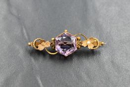 A yellow metal bar brooch stamped 9ct having central hexagonal amethyst in decorative floral mount