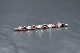 A white metal ruby and diamond bar brooch marked 18ct, the alternating mixed oval cut rubies and