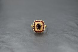 A yellow metal (presumed gold) and garnet ring, the central oval cut garnet in a six claw setting
