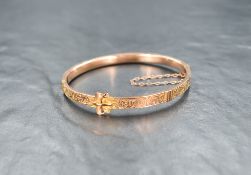 A early 20th Century 9ct rose gold hinged bangle modelled as a belt with scroll decoration,
