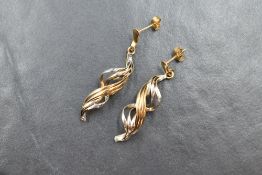 A pair of 9ct two tone gold drop earrings, the twisted ribbons of white and yellow gold with stud