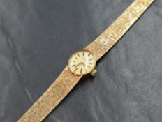 A vintage 9ct gold Caravelle wristwatch, the oval golden dial having baton numerals, on a 9ct gold