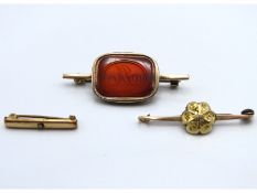 A yellow metal brooch set with carnelian, 45mm wide, twinned with one other yellow metal small bar b