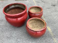A set of three graduated red glazed circular earthenware garden planters, largest diameter 49cm,