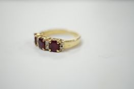 A modern yellow metal and three stone ruby set half hoop ring, with diamond chip spacers, size L,