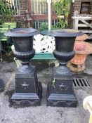 A pair of Victorian style black painted cast iron campana shaped garden urns, on square plinths,