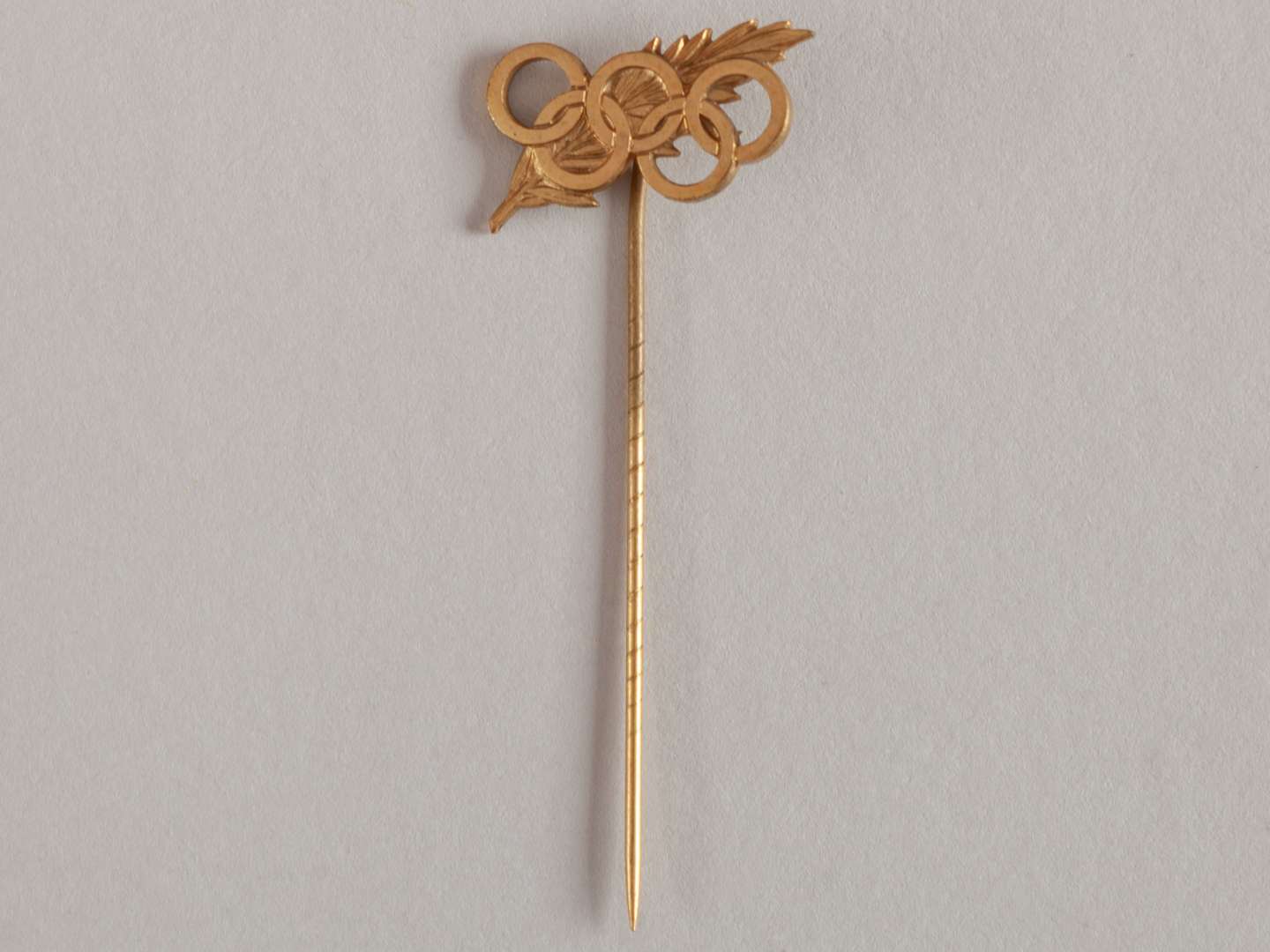 Gilt stick pin commemorating the 50th Anniversary of the International Olympic Committee.