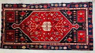 A CAUCASIAN RUG, THE DOUBLE ENDED CENTRAL MOTIF ON A DARK BLUE FIELD.