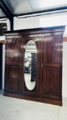 A LARGE EDWARDIAN MAHOGANY TRIPLE WARDROBE WITH CENTRAL OVAL MIRRORED DOOR W 197CM D 57CM H 213CM -