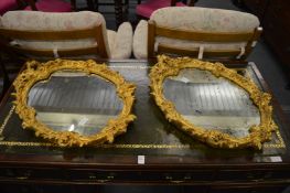 A pair of decorative gilt framed oval wall mirrors.