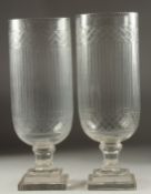 A PAIR OF CUT GLASS HURRICANE LAMPS on square stepped bases. 1ft 4ins high.